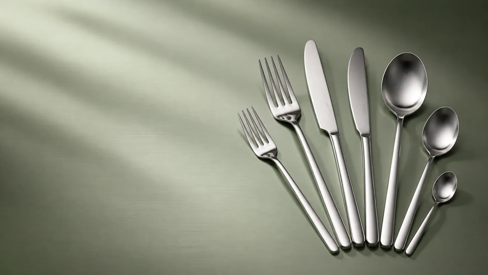 Complete stainless steel flatware collection on a sage surface