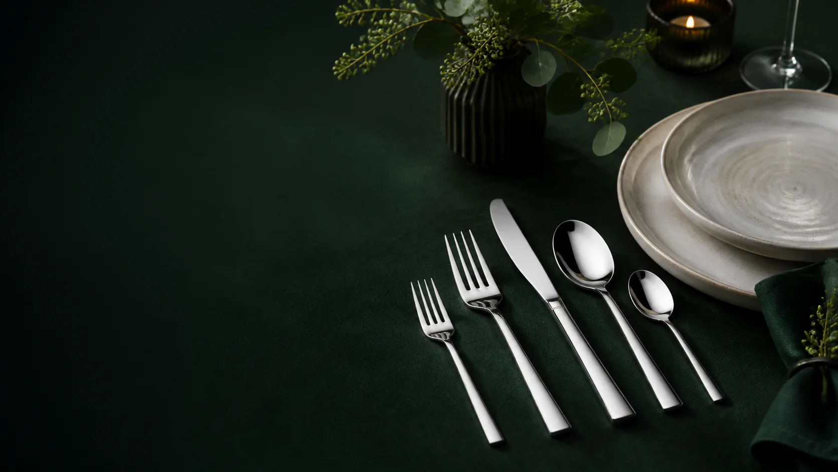 Stainless steel table setting on deep green linen
