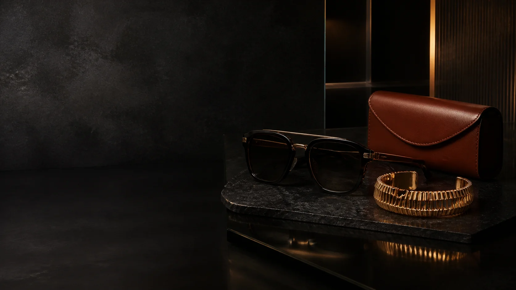 Black eyewear, gold bracelet and cognac leather case on dark stone